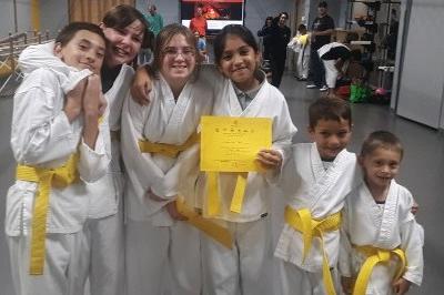 six smiling casually standing young boys and girls showing off new yellow belts