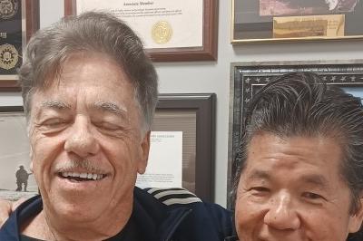 McElroy and Fong posed standing, smiling, arms on shoulders.