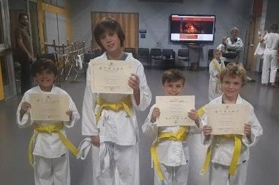 Four young students pose showing off their new yellow belts and related MMAA certificates